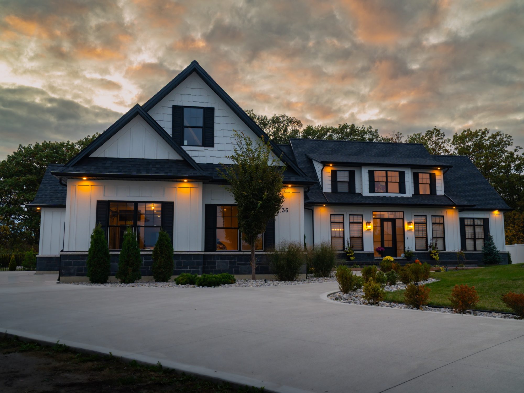 White modern farmhouse with black windows and warm exterior lighting at dusk