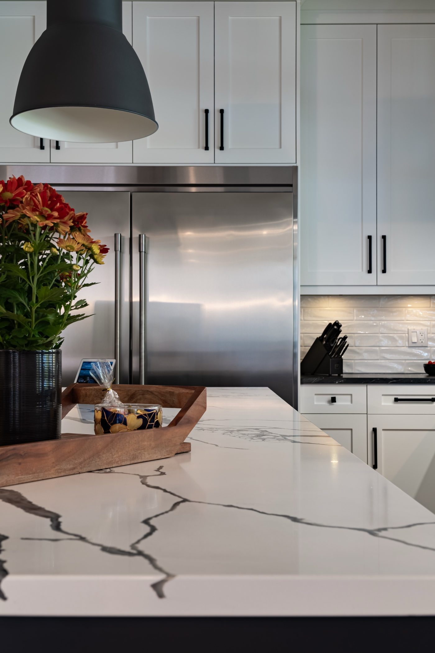 Marble kitchen island with a wooden tray and flowers, a stainless refrigerator and white cabinetry behind