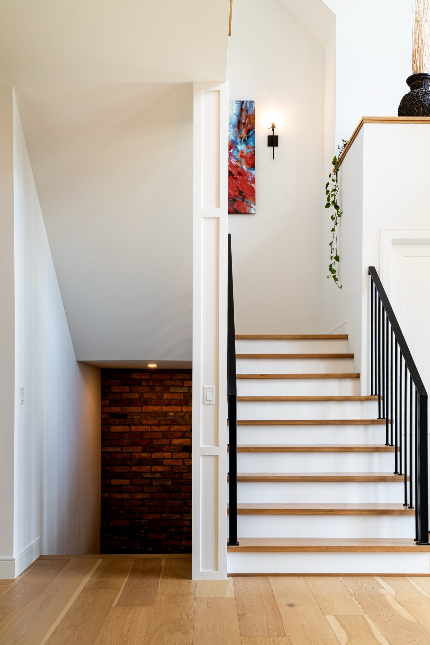 Oak staircase with black iron balusters beside a reclaimed brick wall