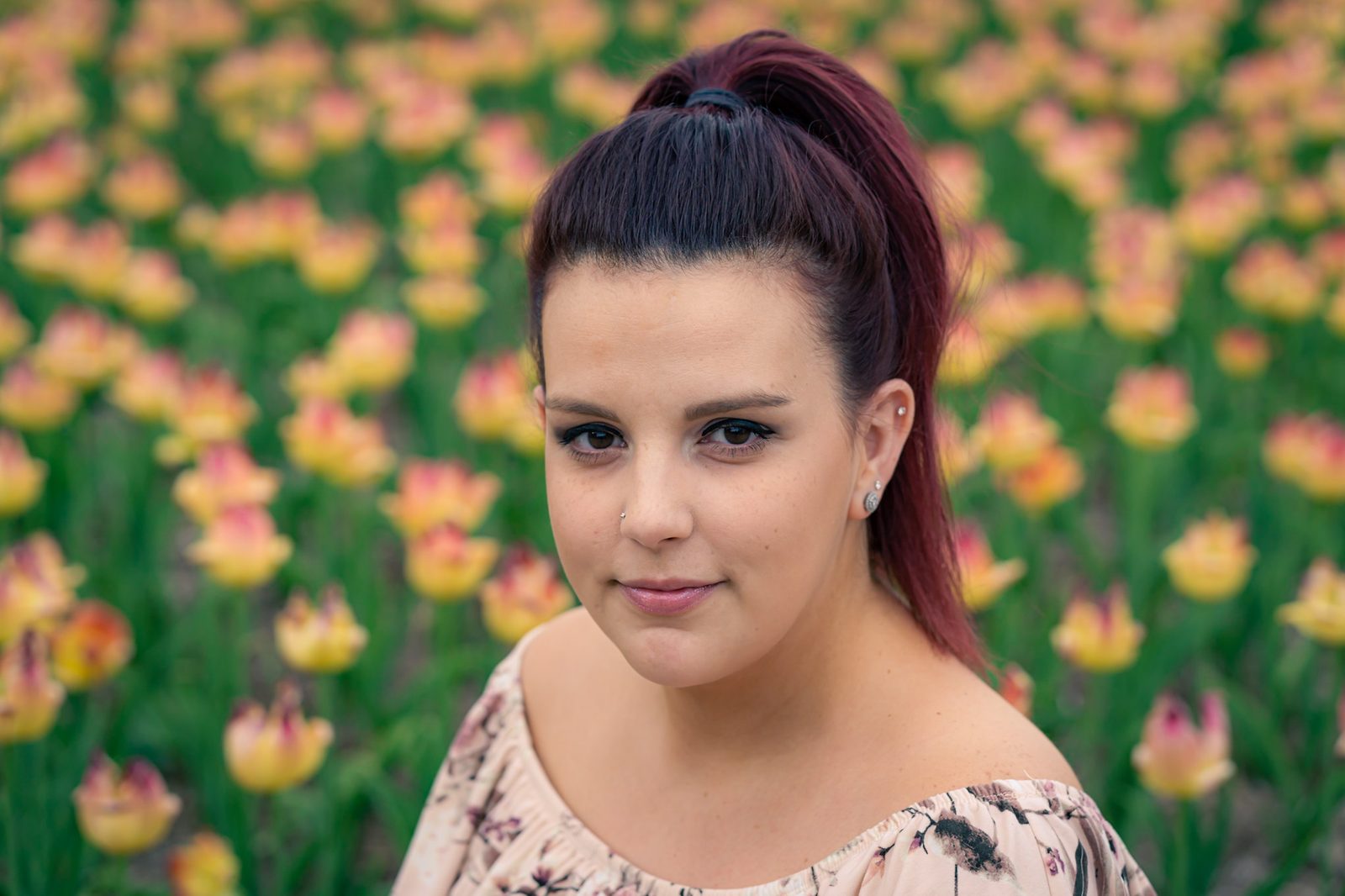 Portrait of a young woman with a high ponytail in front of a field of yellow and pink tulips