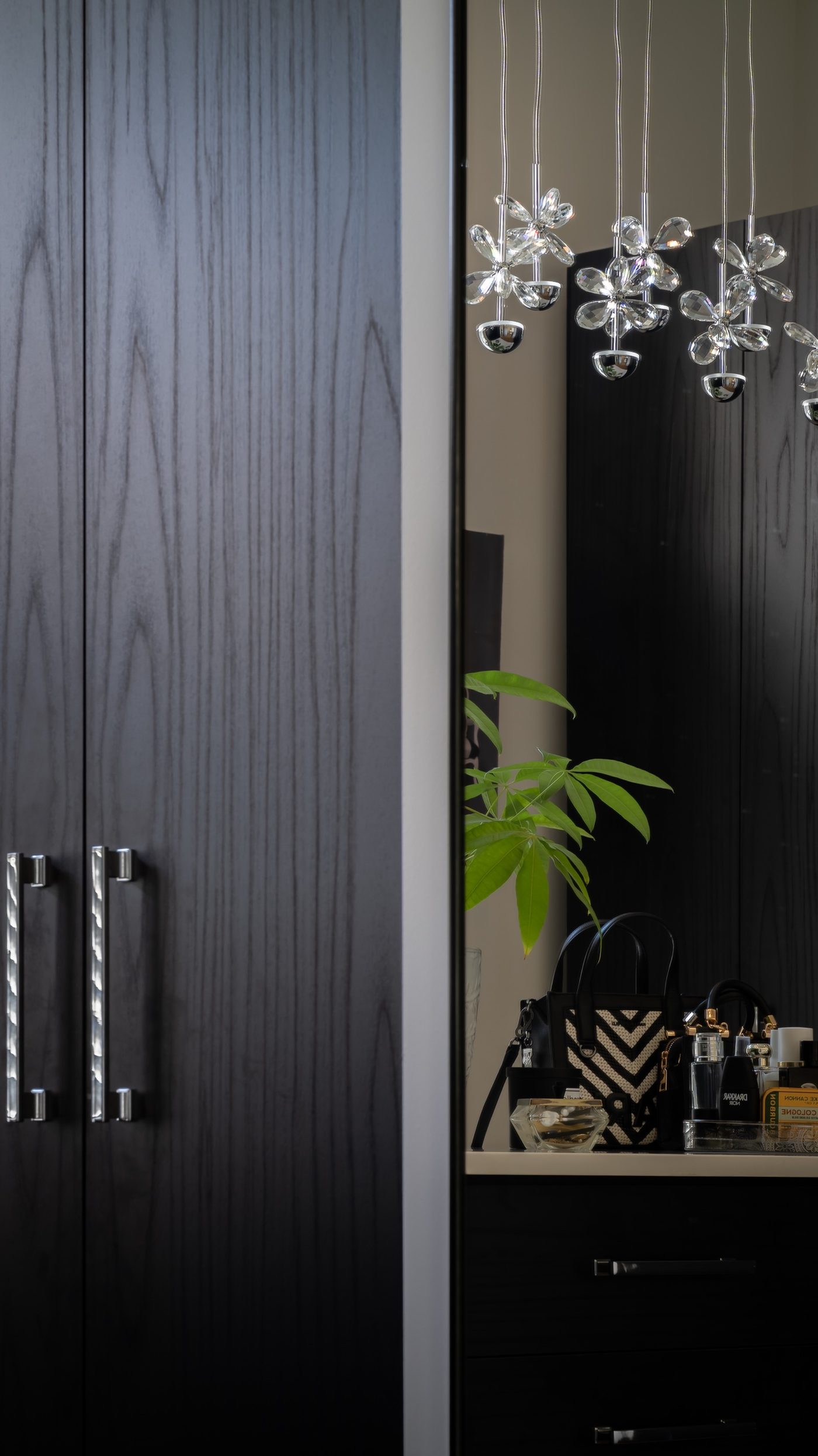 Dark wood-grain wardrobe doors with silver handles beside a mirror reflecting a crystal flower chandelier